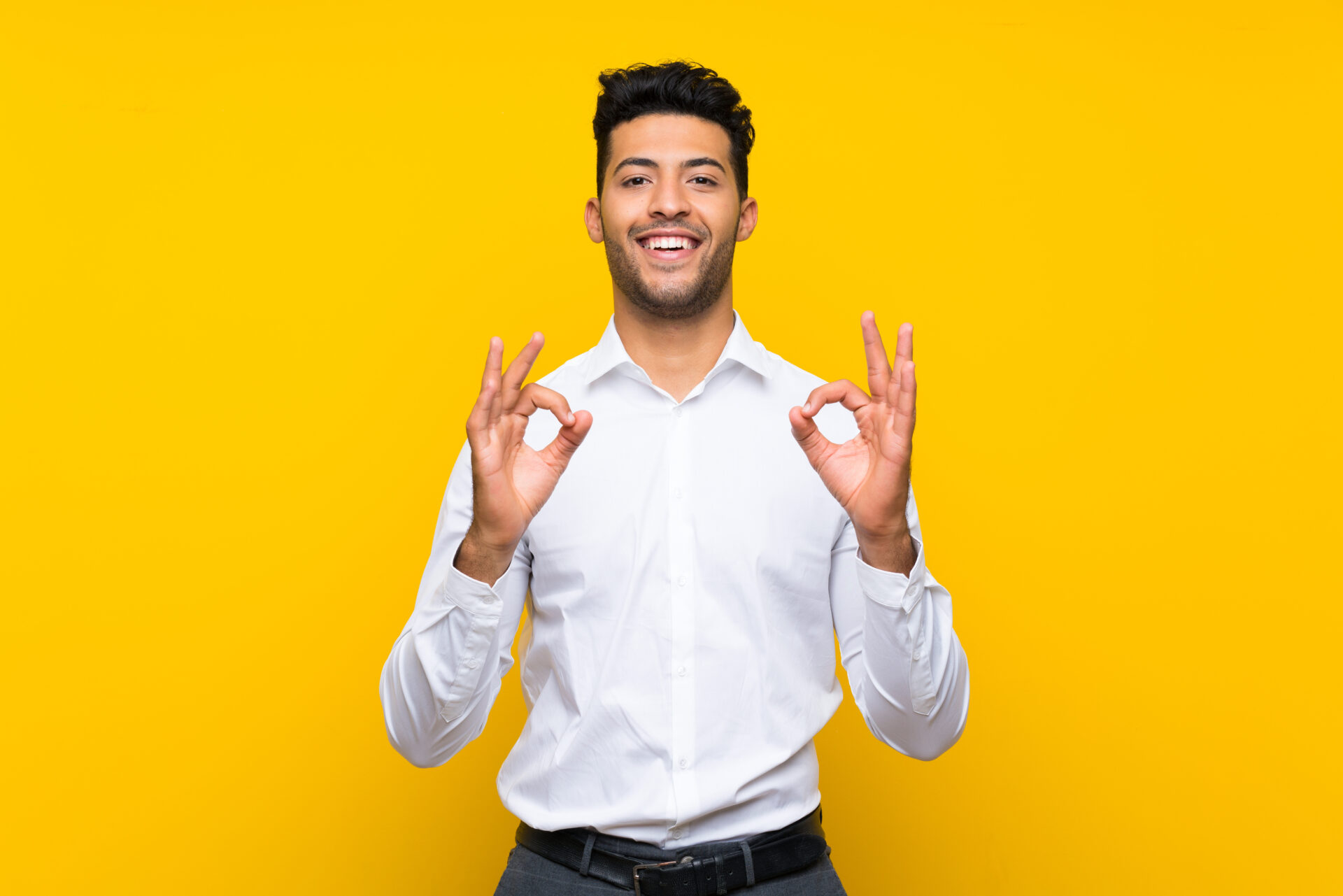 Young man over isolated yellow background showing an ok sign with fingers